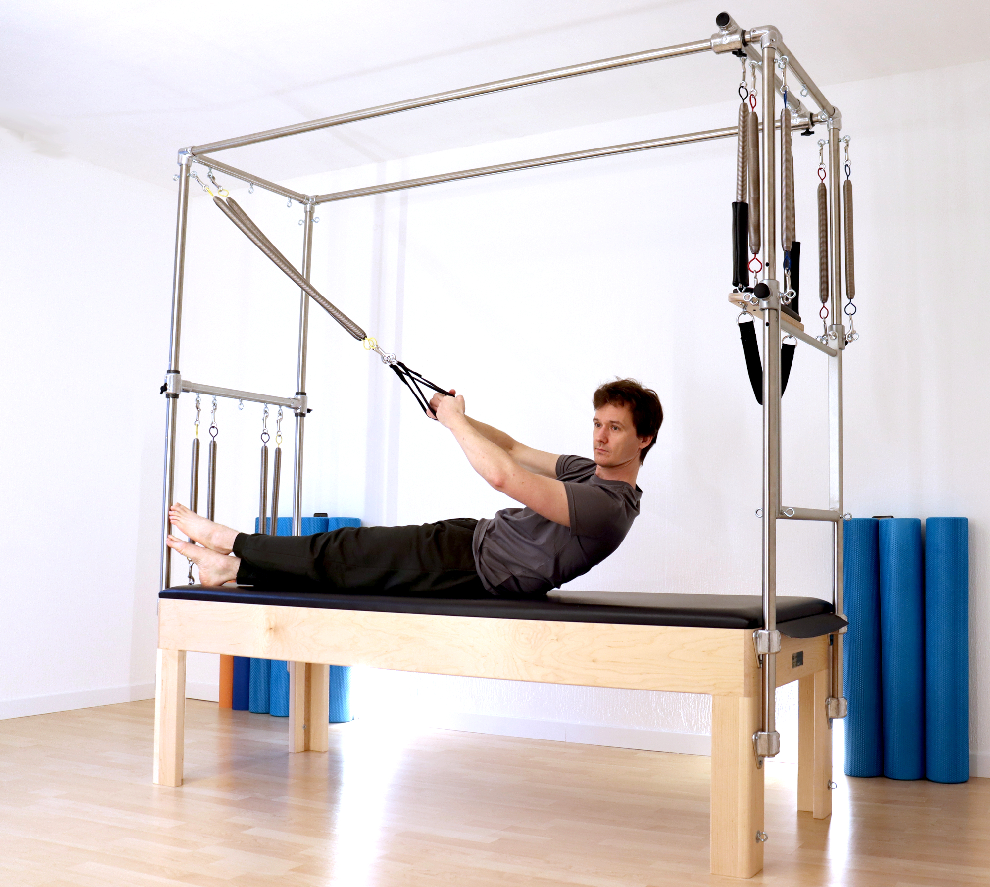 Foto: Pilatestrainer liegt gestreckt und füht Pilates Übung mit einem Cadillac oder Trapez Tisch aus