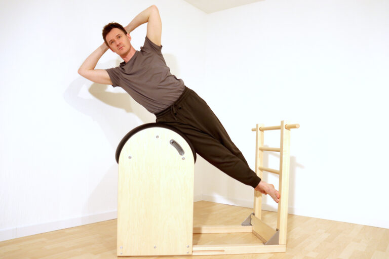 Foto: Mann gestreckter Körper, seitlich als Pilates Übung auf dem Barrel